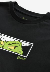 Černé tričko s kulatým výstřihem s grafikou zelené tváře Grinche se žlutýma očima a bílým obláčkovým hovorem.
