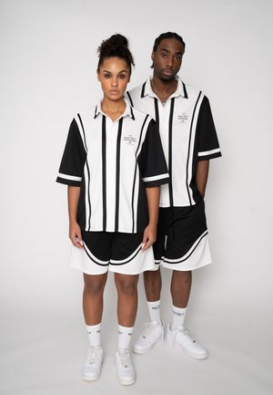 Two people wearing matching black and white striped shirts and shorts standing against a plain light background.