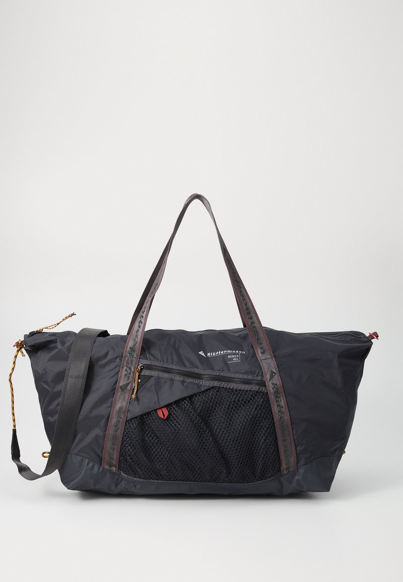 Svart duffelbag med en teksturert mesh-lomme, røde detaljer, dobbelthåndtak og glidelås. Laget av slitesterkt, vannavstøtende materiale.