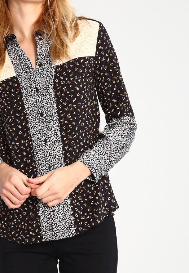 Svart skjorta med knappar och blommönster, med varierande tryck på ärmarna och bröstet. Materialet är lätt och har en slät yta.
