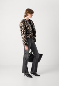 Leopardprint nephaljasen met een ronde kraag, gecombineerd met lichtgrijze flared jeans en zwarte puntige hakken, terwijl ze een zwarte handtas vasthoudt.