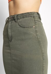 Olivově zelená džínová sukně s vysokým pasem, designem s pěti kapsami, zapínáním na kovový knoflík a kontrastními švy.