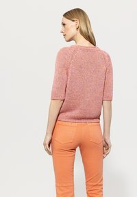 Knit pink and orange short-sleeve top with textured pattern, ribbed neckline, and hem, paired with orange fitted pants and back pockets.
