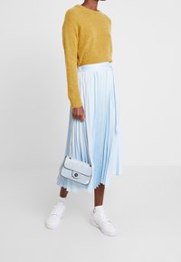 Suéter mostaza, falda plisada azul claro, bolso texturizado azul claro con correa de cadena y zapatillas blancas. Diseño simple y limpio.