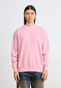 Ροζ φόρμα με στρογγυλή λαιμόκοψη, ριμπ μανσέτες και στρίφωμα. Διαθέτει ένα διακριτικό λογότυπο στο στήθος. Συνδυάζεται με ξεθωριασμένα μπλε τζιν.