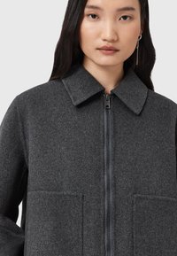 Veste en mélange de laine grise avec un col, une fermeture éclair à l'avant et deux grandes poches plaquées. Texture douce, coupe cintrée et design minimal.
