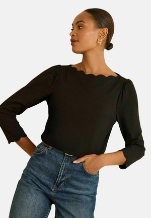 Schwarze Bluse mit einem gewellten Ausschnitt, puffigen Dreiviertelärmeln und glatter Textur, kombiniert mit hochgeschnittenen blauen Jeans.