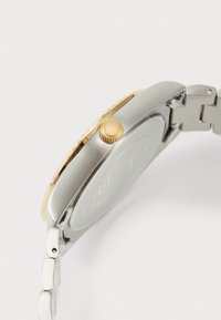 Silver stainless steel watch with gold accents, a textured bezel, and a gold crown. Features a smooth metal band and a polished finish.