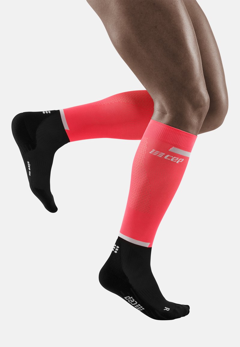 Calze a compressione lunghe fino al ginocchio, con parte superiore rosa brillante e piede nero. Presentano un tessuto testurizzato, un marchio bianco e sezioni del tallone e delle punte di colore contrastante.
