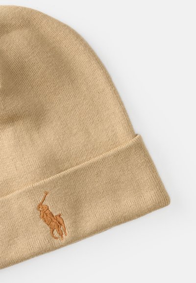 Gorro beanie bege feito de material de malha com uma dobra na barra, apresentando um logotipo bordado em uma cor bege ligeiramente mais escura.