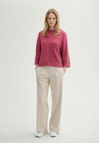 Maglione lavorato a maglia a maniche corte di un rosa intenso con texture a coste; abbinato a pantaloni cream a vita alta e gamba larga e sneakers bianche.