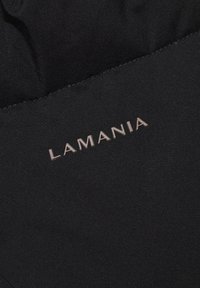 Czarna tkanina o gładkiej fakturze z wytłoczonym, jasnobrązowym napisem "LAMANIA" wzdłuż dolnej krawędzi.