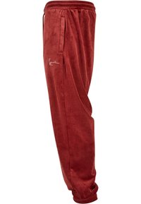 Röda velourbyxor med resårmidja, sidofickor och en liten broderad logotyp. Mjuk textur och avsmalnande bendesign.