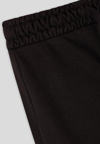 Czarne bawełniane spodnie dresowe charakteryzują się zebranym elastycznym paskiem w talii oraz bocznym szwem, prezentując gładką teksturę i jednolity kolor.