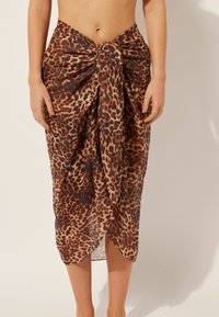 Falda envolvente de estampado de leopardo en una tela ligera y transparente, con un detalle de nudo retorcido en la cintura. El dobladillo crea una silueta fluida.
