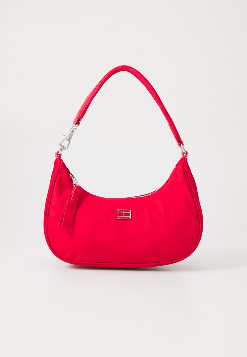Sac à bandoulière en nylon rouge de forme incurvée, avec quincaillerie en métal, fermeture éclair et une petite plaque logo à l'avant. Texture lisse.