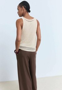 Beige knitted tank top with a diamond pattern and wide armholes, paired with loose brown pants. Captures back view details.
