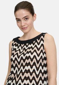 Schwarzes und weißes ärmelloses Oberteil mit einem Zickzackmuster, das einen einfarbigen schwarzen Halsausschnitt und einen leichten, strukturierten Stoff hat.