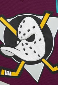 Maschera da hockey bianca con occhi neri e arrabbiati, bastoni da hockey gialli incrociati, posizionata su uno sfondo viola con forme grigie e nere.