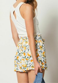 White sleeveless top with a back keyhole cutout, paired with a floral short skirt featuring yellow fruit patterns on a white background.
