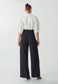 Witte korte mouwen shirt met een relaxte pasvorm, gecombineerd met zwarte wijde broek. Glad materiaal, geen zichtbare patronen of versieringen.