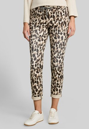 Frau trägt beige-braune, kurz geschnittene Leopardenhose mit umgeschlagenen Säumen, einen hellbeigen Pullover und weiße Turnschuhe.