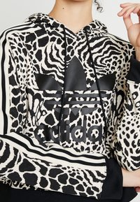 Felpa con cappuccio con stampa animale in bianco e nero, dotata di un grande logo nero nella parte anteriore e maniche nere a righe. Tessuto testurizzato.
