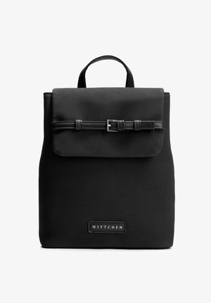 Sac à dos rectangulaire noir avec un rabat fixé par une fine sangle à boucle et une poignée supérieure, marqué du label "WITTCHEN" à l'avant.