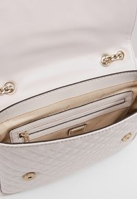 Prošívaná, světle růžová kabelka se zlatými kovovými prvky. Má prostorný interiér se zipovou kapsou a hladkým béžovým podšívkou.