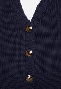 Cardigan lavorato a maglia blu navy con scollo a V, quattro grandi bottoni rotondi con finitura lucida e un motivo a costine sulla stoffa.