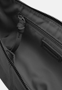 Pochette in pelle nera con una superficie liscia, chiusura con zip, tasca interna e etichetta con la scritta "FRED BRUDER." Interno foderato con materiale scuro.