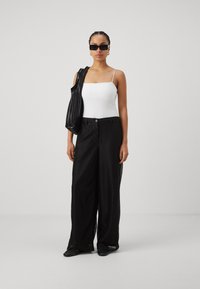 Sorte vide benbukser i mesh med høy midje og en lys hvit tettsittende tanktop. Tilbehør inkluderer en teksturert svart veske og solbriller.