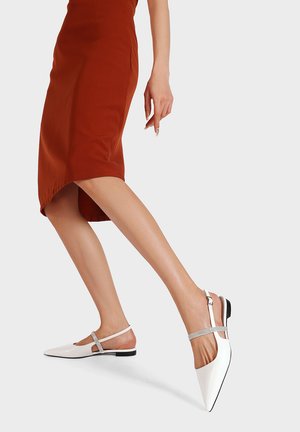 Scarpe slingback bianche con punta a punta, dotate di una fascia d'accento argentata e tacco nero basso, indossate con una gonna a tubino color ruggine. Finitura liscia.