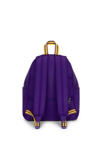 Mochila morada con correas acolchadas para los hombros, un asa superior con detalles en amarillo y un bolsillo lateral con cremallera. Textura de tela suave.