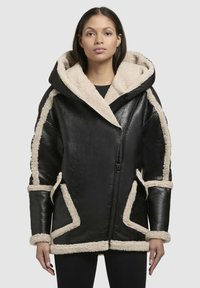 Sort læderjakke med en stor pelsforet hætte, cremefarvede faux shearling-detaljer langs sømmene og mansjetterne, med en frontlynlås.