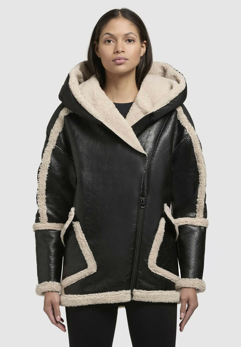 Sort læderjakke med en stor pelsforet hætte, cremefarvede faux shearling-detaljer langs sømmene og mansjetterne, med en frontlynlås.
