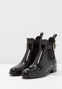 Bottes Chelsea en cuir verni noir avec des panneaux latéraux élastiques, des accents en métal doré, des bouts ronds et de petits talons carrés.