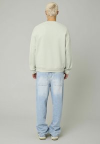 Sweat-shirt vert clair à col rond et manches longues, associé à un jean bleu clair à coupe décontractée avec un effet délavé.