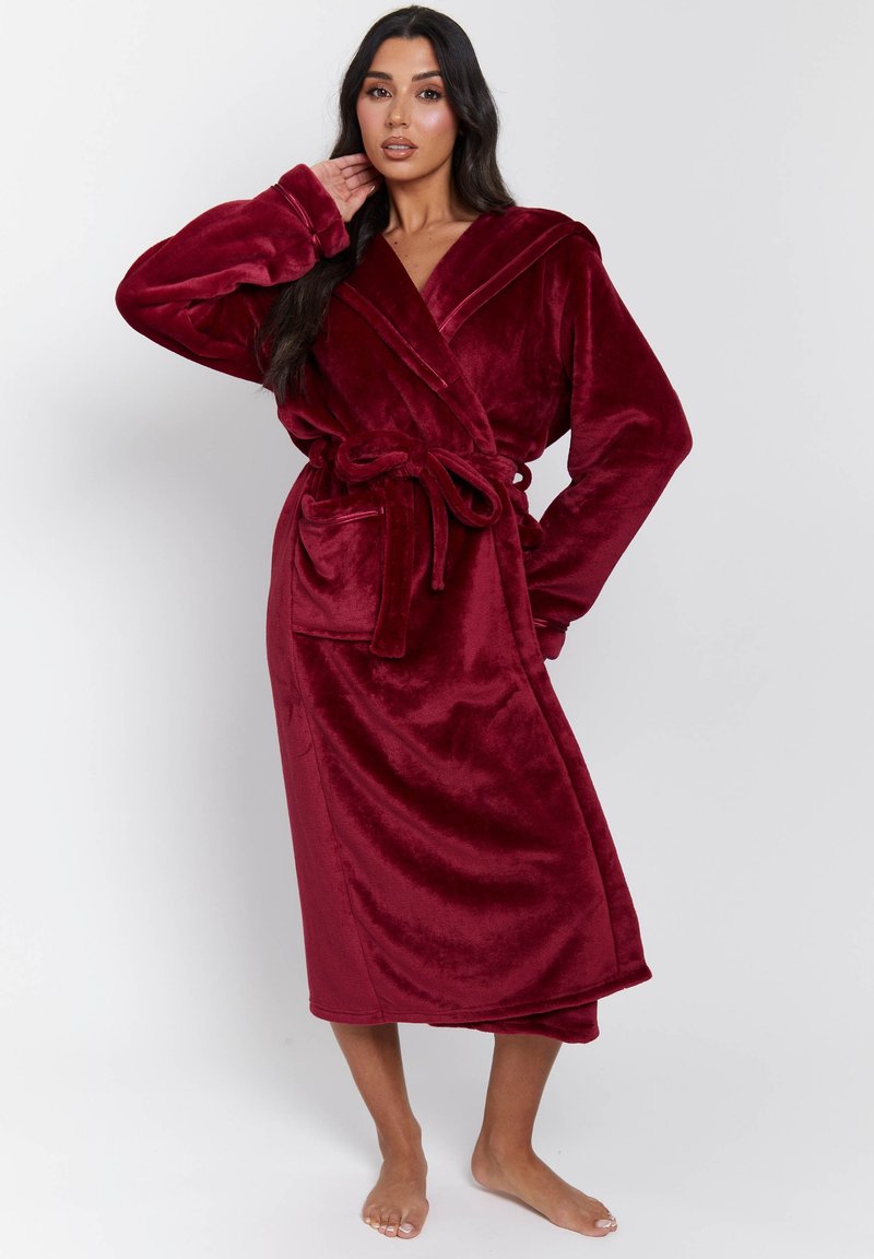 Burgundy plyschrock med sjalkrage, bälte i midjan, långa ärmar och fickor. Mjuk textur och design som når mitt på vaden.