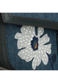Tomaia in denim con fiore grigio ricamato con pois bianchi, centro blu scuro e dettagli arancioni su uno sfondo blu testurizzato.