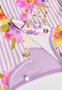 Gėlėmis marginta medžiaga pastelinių spalvų su dryžuotu levandų fonu; turi spaustukus ir minkštą tekstūrą. Papuoštos kraštinės purpurine spalva.