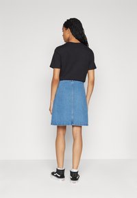 Zwart T-shirt met korte mouwen gecombineerd met een lichtblauwe spijkerrok, met een rits aan de achterkant en een knie-lange snit, gedragen met zwarte hoge sneakers.