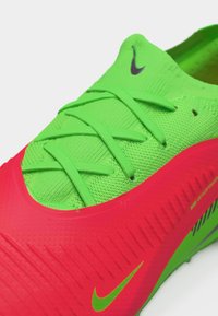 Πράσινο και κόκκινο αθλητικό παπούτσι Nike με ενσωματωμένα κορδόνια και ορατά λογότυπα Nike Swoosh στη γλώσσα και στο πλάι.