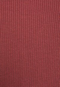 Roter Strickstoff mit einem engen, strukturierten Muster. Das Material wirkt weich und hat eine gleichmäßige Webart.