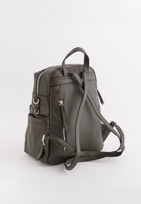 Sac à dos en cuir vert foncé avec une surface texturée, deux bretelles, une poignée supérieure et des poches zippées à l'avant et sur le côté.