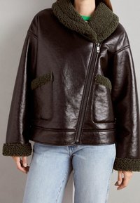 Veste en cuir noir avec col et poignets en velours texturé vert, dotée d'une fermeture éclair à l'avant et de poches latérales. Coupe ajustée.