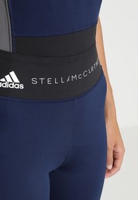 Marina sporttights med svart elastisk midja som har texten "STELLAMCCARTNEY" och Adidas-logotypen. Slät tygkvalitet med en figurnära design.