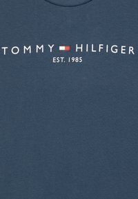 M�ørkeblå bomulds T-shirt med "TOMMY HILFIGER" logo i hvid, med rød og hvid rektangulær grafik; etableringsår 1985 trykt nedenfor.