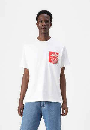 Weißes Baumwoll-T-Shirt mit einem roten Taschenmotiv und floralen Grafiken. Kurze Ärmel und runder Halsausschnitt, lockere Passform. Sichtbare blaue Jeansshorts.
