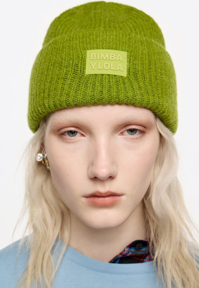 Gorro de punto verde con textura acanalada y una etiqueta rectangular de logo que dice "BIMBA Y LOLO" en verde claro.